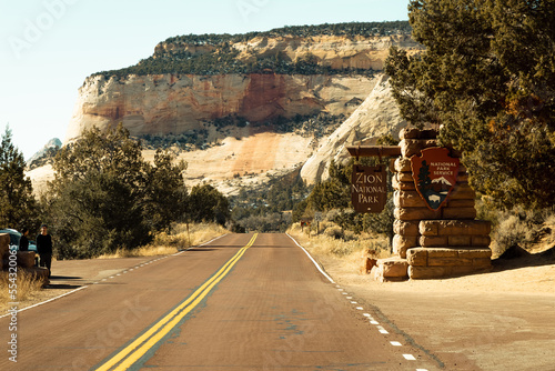 The main entrance sign into zion national park as you drive into the east entrance of the park. People stand infront of sign to get a photo before entering NPS.
