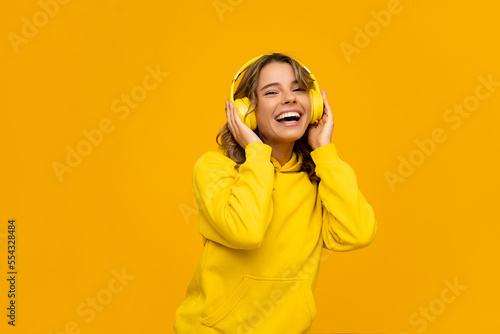 smiling attractive woman listening to music in headphones on yellow background