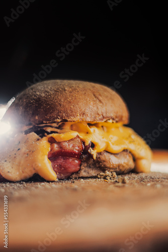 Delicious hamburger, with homemade meat, lots of cheese and bacon, with a black background and fire scene, melting cheese. 