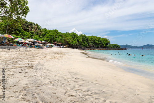 BALI, INDONESIA - NOVEMBER 6, 2022: Bias Tugel beach at the south of Bali island. Many tourists swimming in blue ocean water. White sand and rock shore.