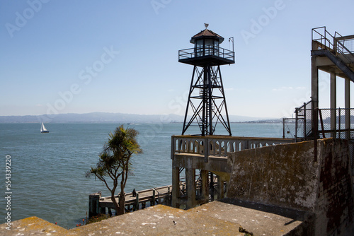 A watchtower on Alcatraz Island, and a scenic view of the water and a sailboat off shore.; Alcatraz Federal Penitentiary, Alcatraz Island, San Francisco Bay, California photo