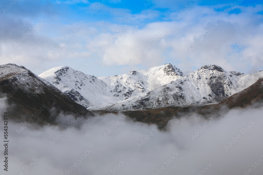 Clouds below and above the ridgeline create islands of mountains with fresh snow on them, on a sunny, blue sky, autumn day in Hatcher Pass, Talkeetna Mountains; Alaska, United States of America Clouds below and above the ridgeline create islands of mountains with fresh snow on them, on a sunny, blue sky, autumn day in Hatcher Pass, Talkeetna Mountains; Alaska, United States of America