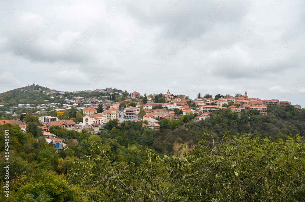 View of the picturesque buildings of the city of Sighnaghi on the hill with colored autumn leaves and trees at foggy day. Georgia