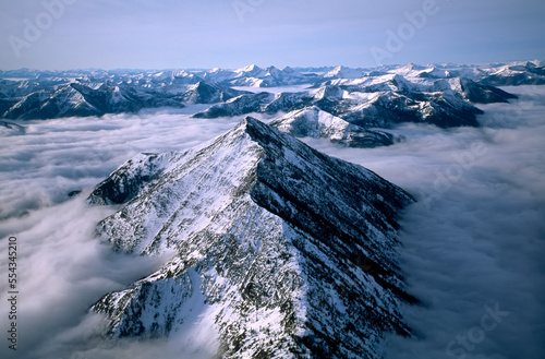 Aerial view of Montana's Rocky Mountain Front, with snowy Rocky Mountains peaks above the clouds; Montana, United States of America