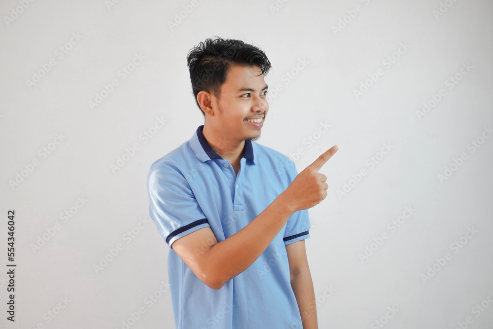 smiling asian man with fingers pointing to the side wearing blue t shirt isolated on white background smiling asian man with fingers pointing to the side wearing blue t shirt isolated on white background