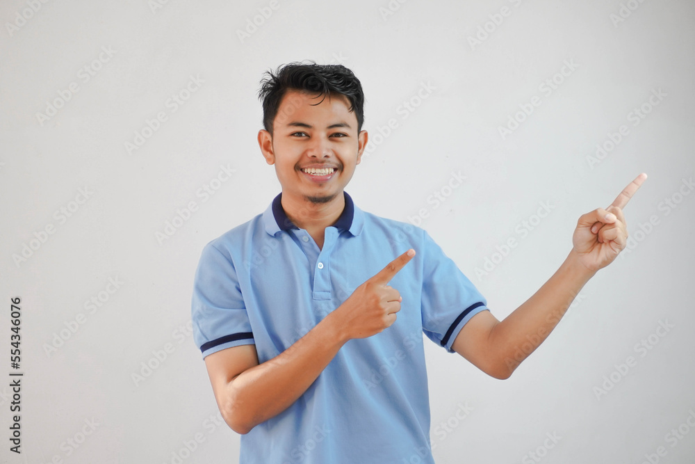 smiling asian man with fingers pointing to the side wearing blue t shirt isolated on white background smiling asian man with fingers pointing to the side wearing blue t shirt isolated on white background