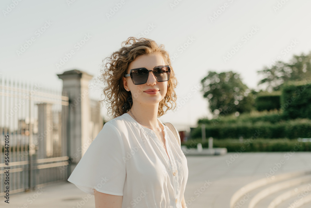 A woman with curly hair in sunglasses is posing in the park