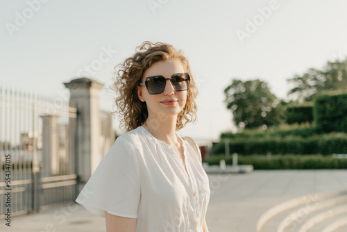 Obraz na płótnie A woman with curly hair in sunglasses is posing in the park w salonie