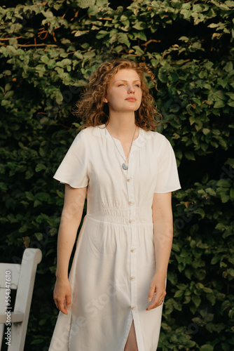 A woman with curly hair is posing in the garden in the evening.