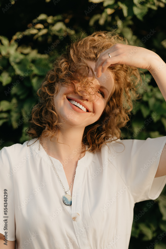 A woman with curly hair is posing in the park at the sunset.