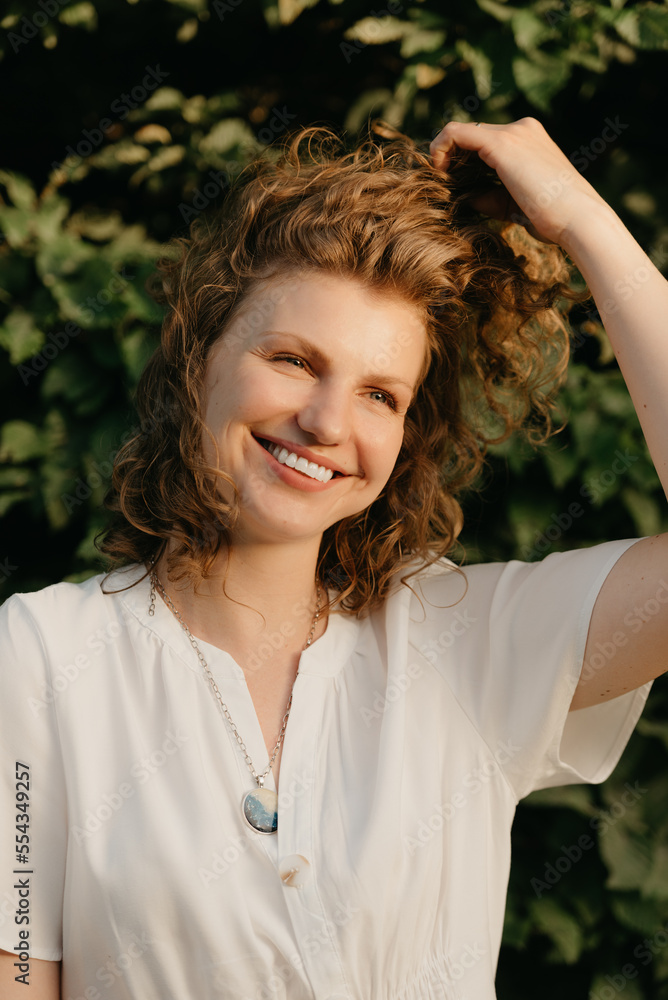 A woman with curly hair is posing in the park at the sunset.