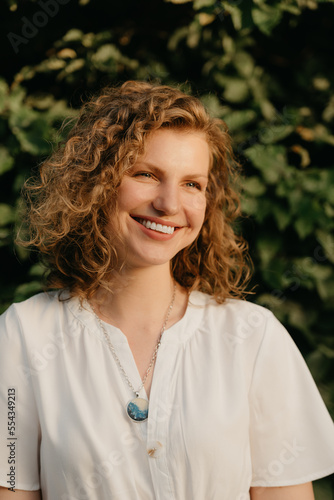 A woman with curly hair is posing in the park at the sunset.