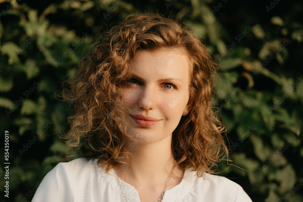 A woman with curly hair is posing in the park at the sunset.