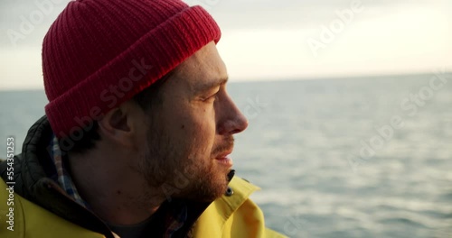 A sailor sits on a boat and smilingly looks at a lighthouse in the distance photo