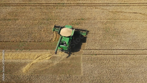 Combine harvester harvests on a summer field. The combine harvests wheat. Agricultural farm for growing wheat. Aerial photography of John Deere harvester