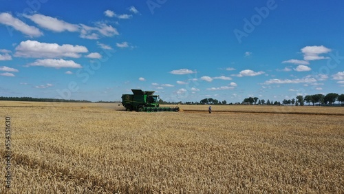 Nesvish district, Belarus - 29.07.2022: A John Deere harvester with the logo of the Nesvizh Agricultural Complex harvests wheat. The combiner-controller walks in front of the combine across the field.