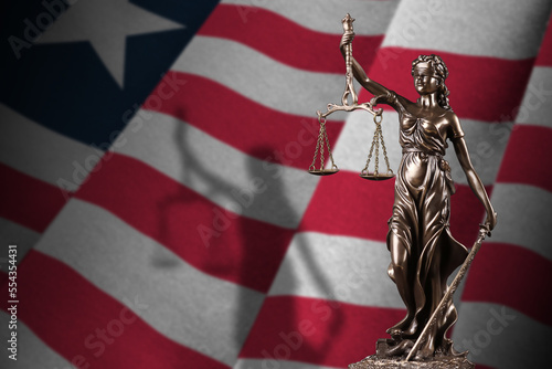 Liberia flag with statue of lady justice and judicial scales in dark room. Concept of judgement and punishment, background for jury topics photo