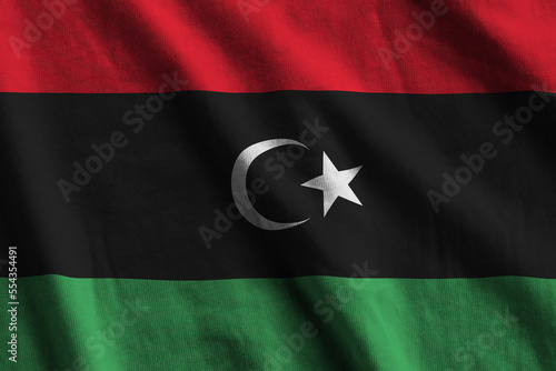 Libya flag with big folds waving close up under the studio light indoors. The official symbols and colors in fabric banner