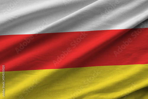 South Ossetia flag with big folds waving close up under the studio light indoors. The official symbols and colors in fabric banner photo