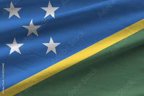 Solomon Islands flag with big folds waving close up under the studio light indoors. The official symbols and colors in fabric banner photo
