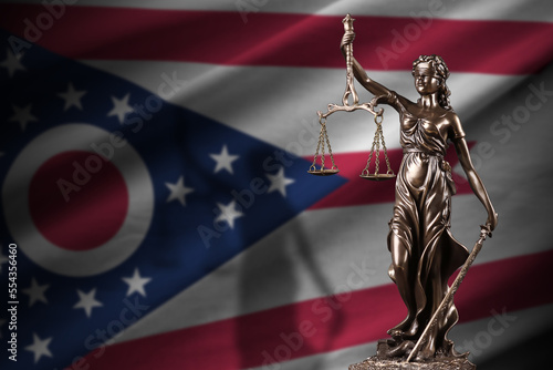 Ohio US state flag with statue of lady justice and judicial scales in dark room. Concept of judgement and punishment, background for jury topics photo