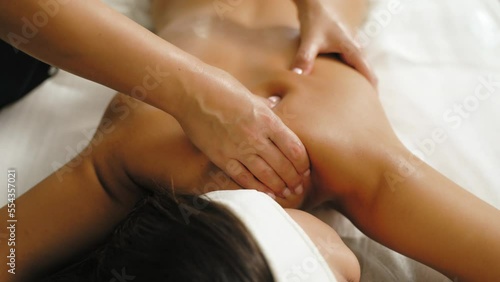 Beauty and health concept. SPA day. Indoor shot of relaxed and positive attractive Asian woman on her stomach during relaxing massage performed by unrecognizable caucasian massage therapist. High photo