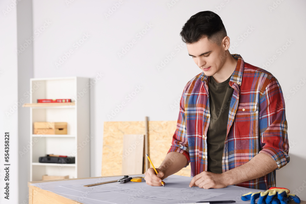 Young handyman working with blueprints at table in room