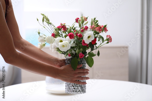 Woman and vase with beautiful flowers on white table in room, closeup