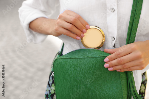 Woman taking cosmetic pocket mirror from bag outdoors, closeup