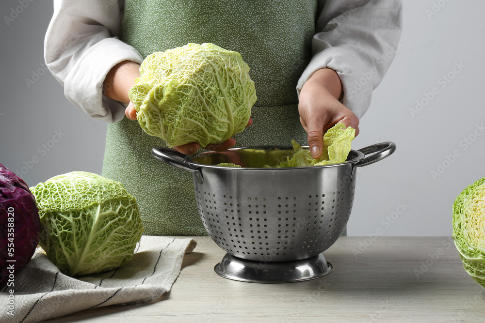Woman putting leaf from fresh savoy cabbage at wooden table, closeup - obrazy, fototapety, plakaty 