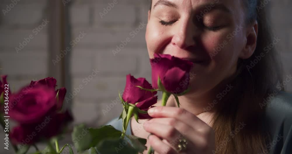 An attractive woman smells a bouquet of red roses and a smile appears on her face. Close up shot. An attractive woman smells a bouquet of red roses and a smile appears on her face. Close up shot.