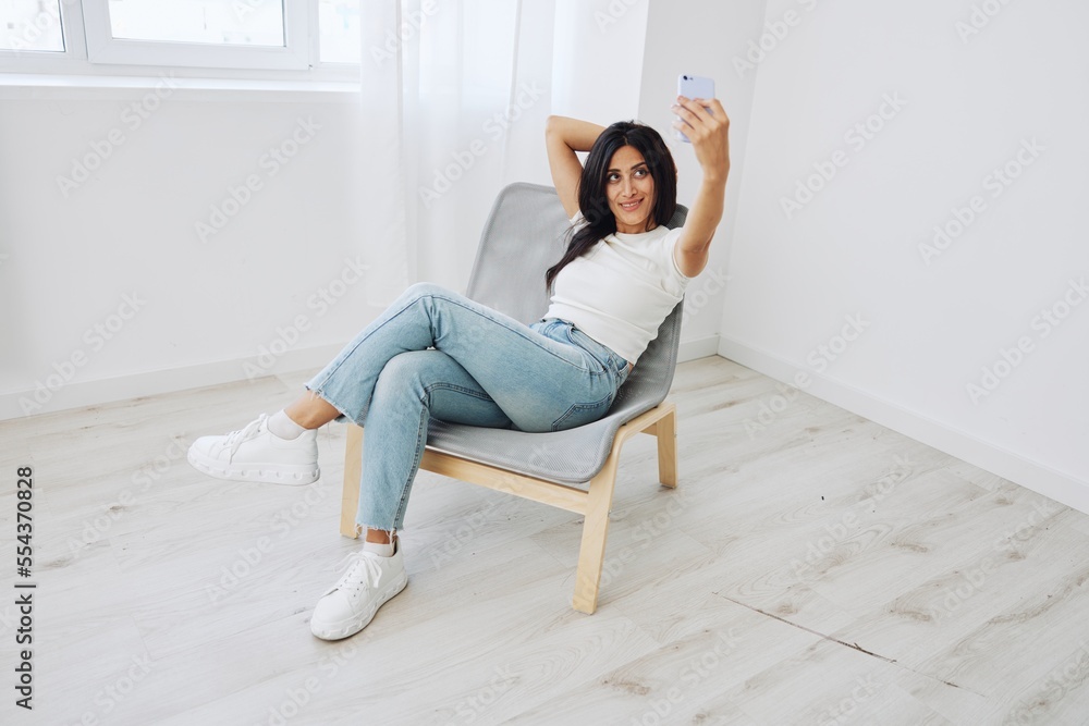 A woman with a phone sits on a chair in jeans and a T-shirt and takes pictures of herself on her phone camera, blogger and selfies A woman with a phone sits on a chair in jeans and a T-shirt and takes pictures of herself on her phone camera, blogger and selfies