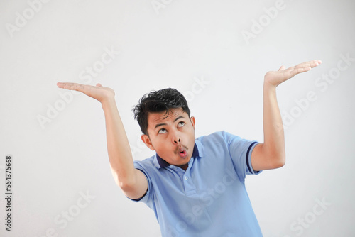 young asian man acting like he's holding up something heavy, but it's just empty copy space wearing blue t shirt isolated on white background. shocked face