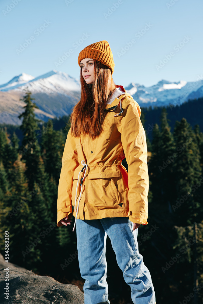 Young woman full-length hiker in yellow raincoat running and walking on a mountain trip in the fall and hiking in the mountains at sunset freedom