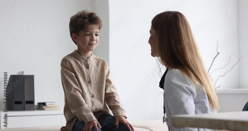 Friendly female doctor or nurse in white coat give high five to little boy during consultation in clinic. Smiling kid patient celebrate successful treatment, finish meeting with pediatrist at hospital Friendly female doctor or nurse in white coat give high five to little boy during consultation in clinic. Smiling kid patient celebrate successful treatment, finish meeting with pediatrist at hospital