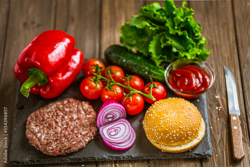 High angle view of ingredients for classic beef burger on stone board with knife. Selective focus. High angle view of ingredients for classic beef burger on stone board with knife. Selective focus.