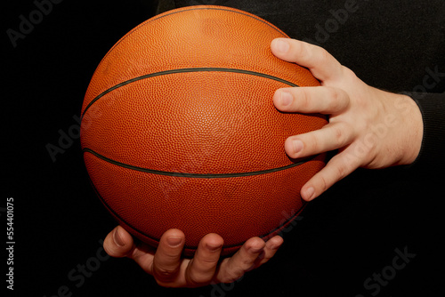 A basketball lies on one hand and the other holds it close-up dark background.. © Александр Ланевский