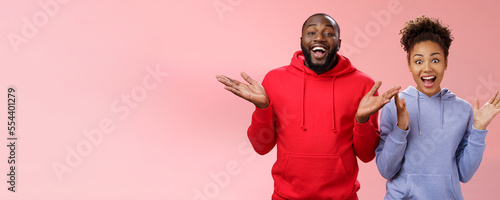 Guys receive nice surprise. Two attractive carefree surprised happy african man woman clapping hands joyfully greeting welcoming guests inviting people joing party standing friendly pink background photo