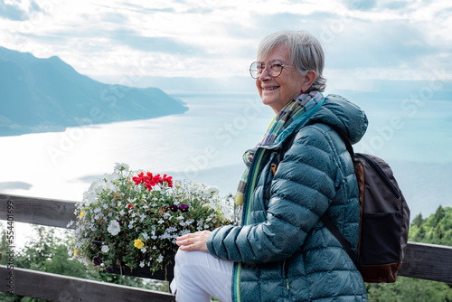 Active elderly traveler woman with backpack admiring the landscape of Lake Geneva from the Sonchaux pass, copy space photo