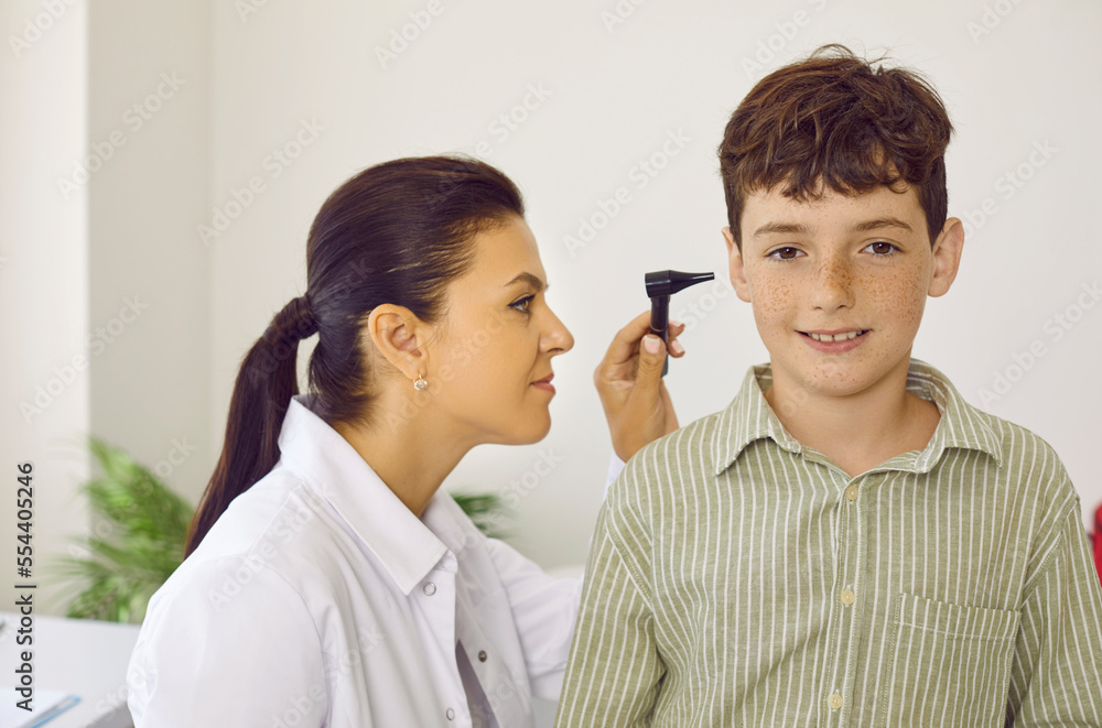 Female otorhinolaryngologist uses otoscope to examine little boy's ear during medical examination in hospital. Diagnostics and treatment of diseases of ear, throat, nose in pediatric practice concept. Female otorhinolaryngologist uses otoscope to examine little boy's ear during medical examination in hospital. Diagnostics and treatment of diseases of ear, throat, nose in pediatric practice concept.