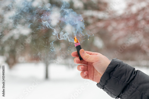 Burning Firecracker in a Hand. Guy Holding a Petard Outdoors in Winter at Daytime. Loud and Dangerous New Year's Entertainment. Hooliganism with Pyrotechnics. Noise of Firecrackers in Public Places