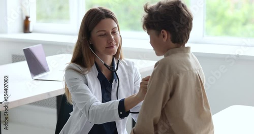 Friendly female pediatrician in white coat examining little 8s boy, auscultate heartbeat of child with stethoscope in her office in clinic or hospital during patient visit. Health check up, medicine