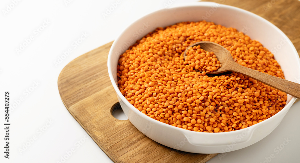 Dry uncooked red lentil groats in a white dish, wooden board, spoon, on a white background, close-up Dry uncooked red lentil groats in a white dish, wooden board, spoon, on a white background, close-up