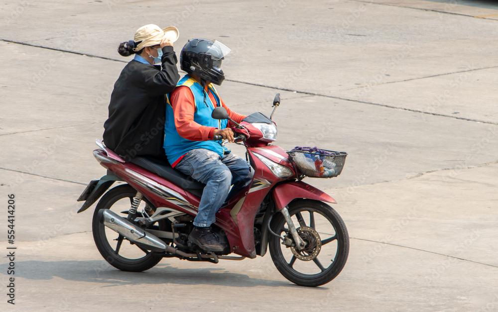 A taxi driver on a motorcycle rides with a woman. The moto-taxi carry a passenger