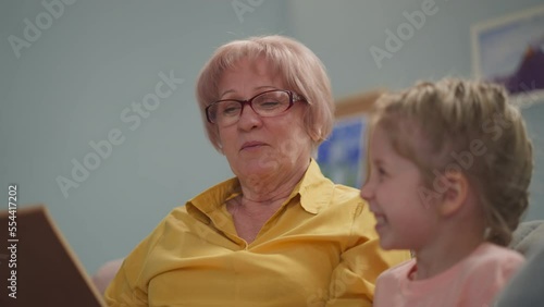 Granny reads fairy tale as actress to happy little child in living room closeup. Grandmother and preschooler girl have fun at home. Family generations