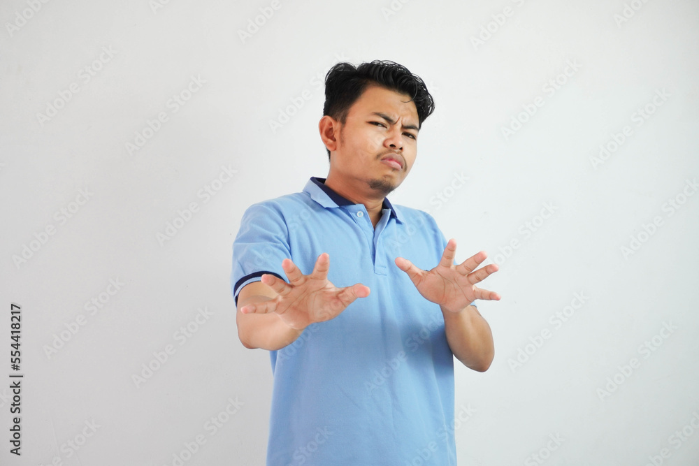 Attractive Asian man with hand gesture pose rejection or prohibition while pointing to copy space by his front wearing blue t shirt isolated on white background Attractive Asian man with hand gesture pose rejection or prohibition while pointing to copy space by his front wearing blue t shirt isolated on white background
