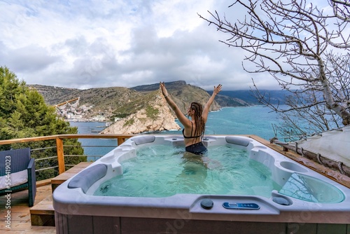 Outdoor jacuzzi with mountain and sea views. A woman in a black swimsuit is relaxing in the hotel pool, admiring the view