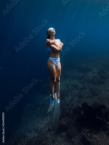 Woman freediver in white bikini with white fins glides underwater in tropical blue ocean