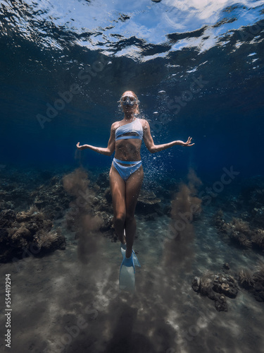 Woman freediver in bikini with sand in hands glides underwater in blue ocean © artifirsov