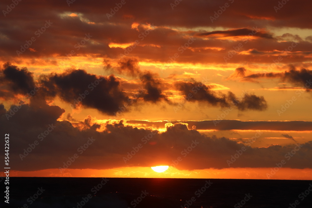 Sunrise producing a golden glow affect upon the passing clouds enhanced by the dark cooling ocean